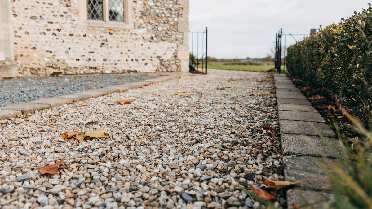Pale loose gravel edged with gray setts running alongside an old stone cottage wall