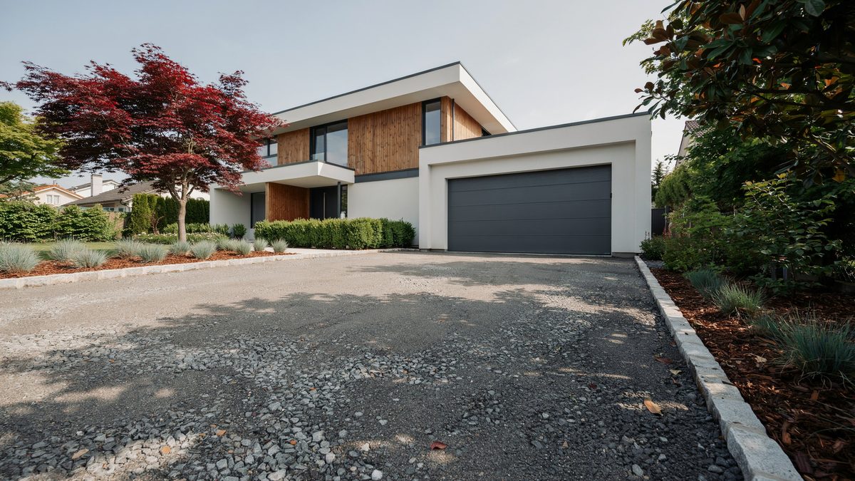 Gray tar and chip driveway leading to a two car garage past a red japanese maple