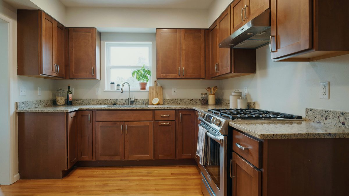 Medium sized kitchen in cherry stained cabinets with speckled granite counters and gas range