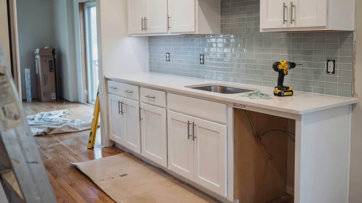Kitchen renovation in progress with new quartz counter, green glass tile and drop cloths