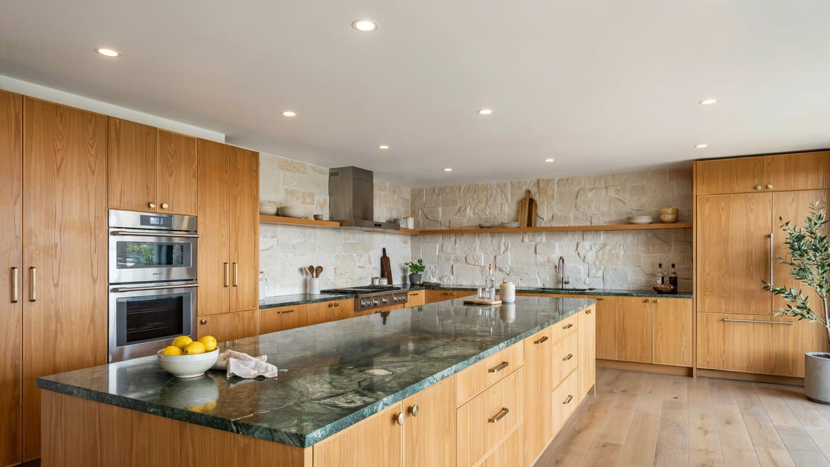 Long light oak kitchen island with mottled Brazilian green granite surface