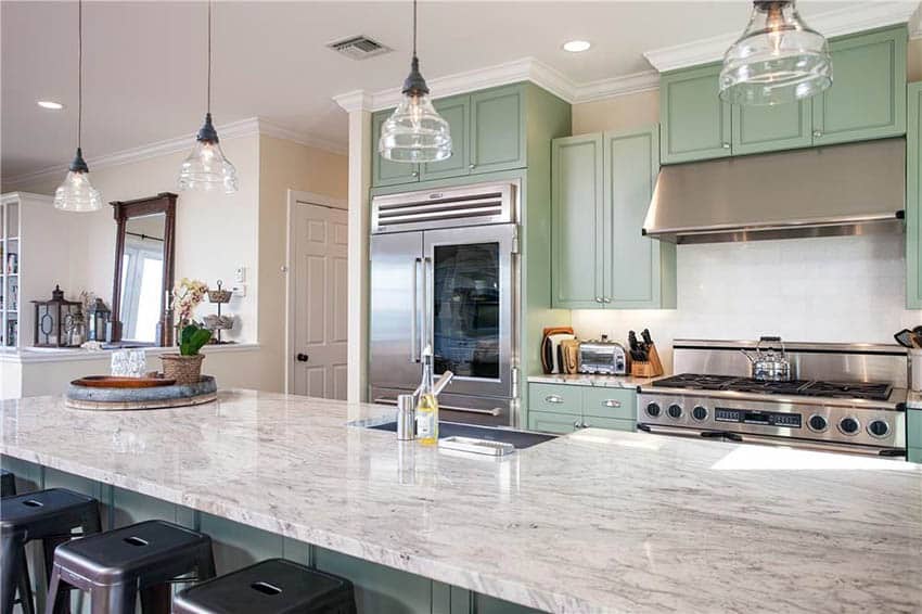 Kitchen with sage green cabinets, white granite countertops and pendant lights over island