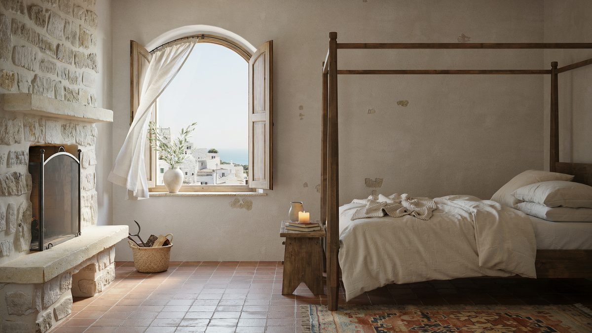 Rough stone hearth with an iron screen beside an arched window over the sea