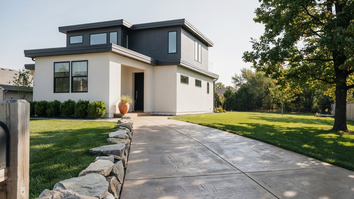 Concrete driveway poured in large panels with a low rough rock wall dividing it from the lawn