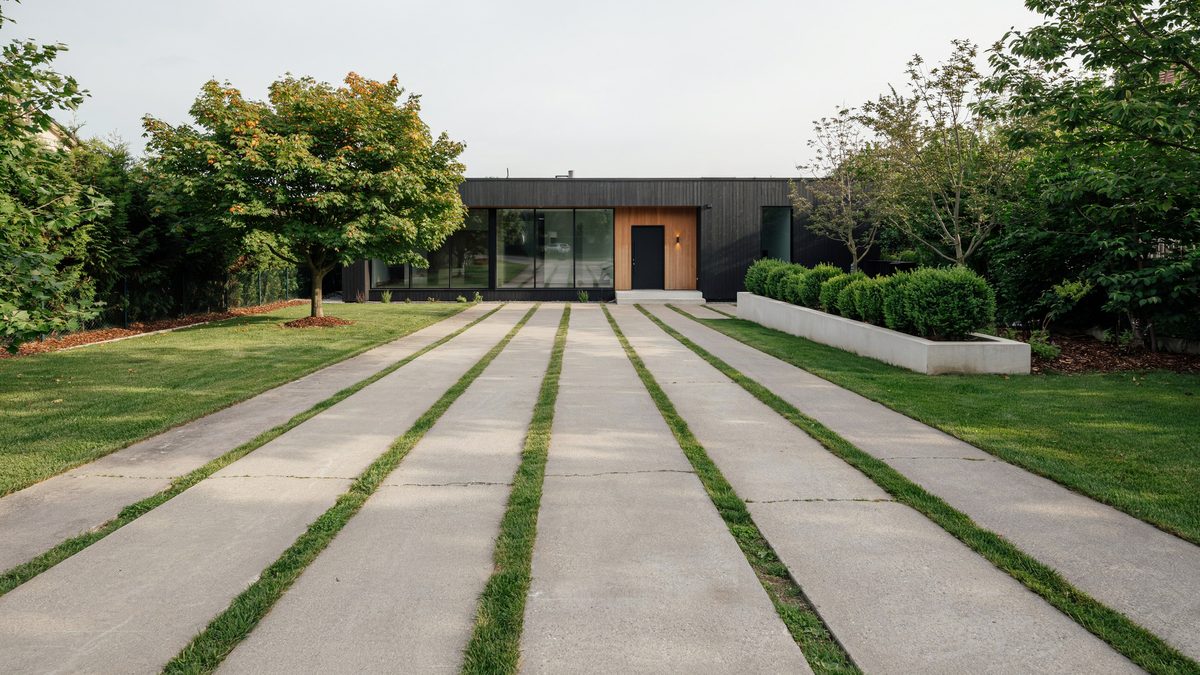 Long concrete strips separated by ribbons of green grass leading to a dark timber house