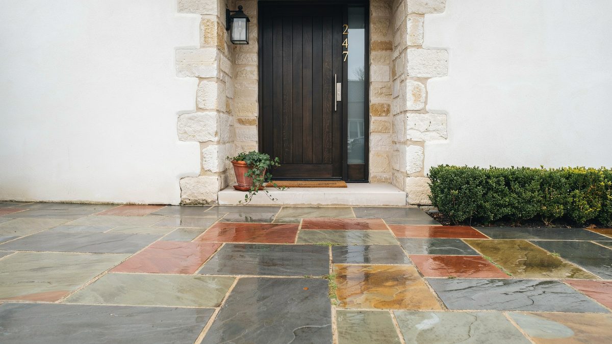 Multicolor slate flagstone paving in rust, gray and green at a stone framed front door
