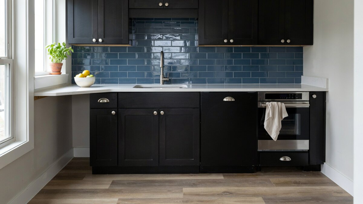 Blue glass subway backsplash lifting black shaker fronts near a bright window