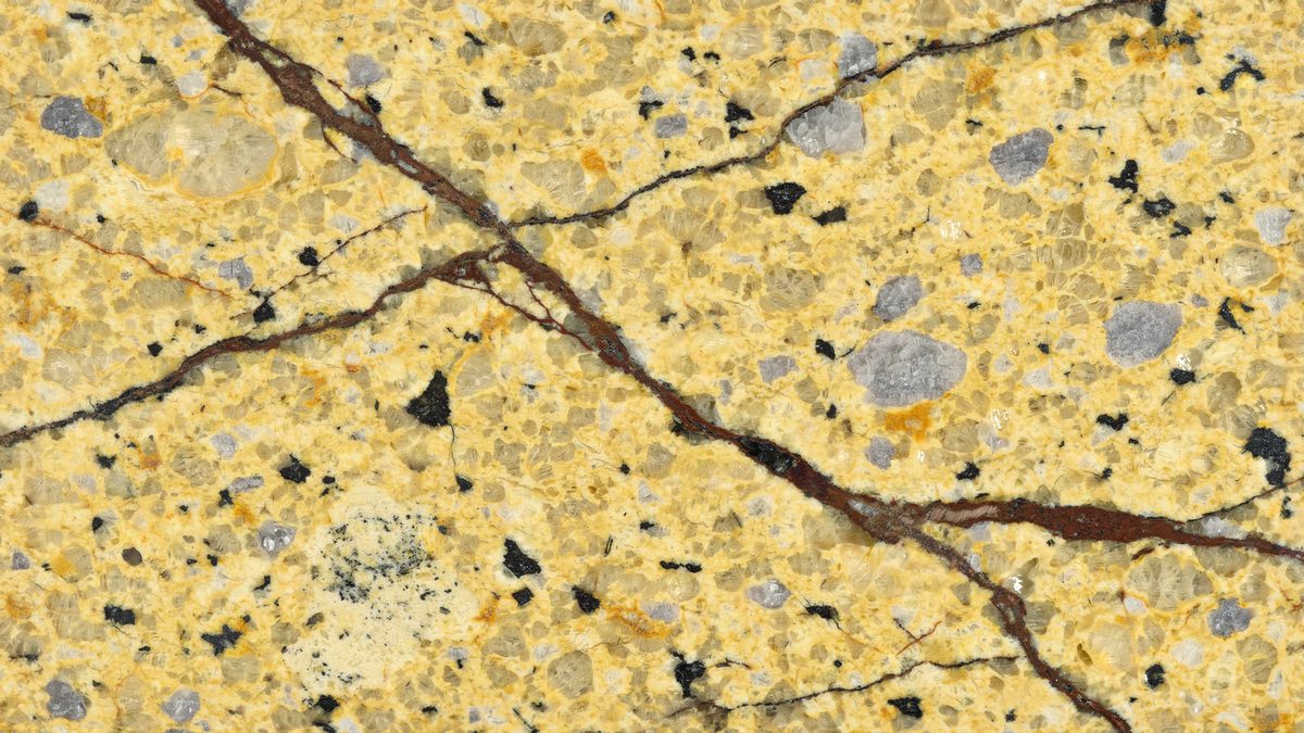 Golden yellow stone dotted with black flecks and split by dark brown veins