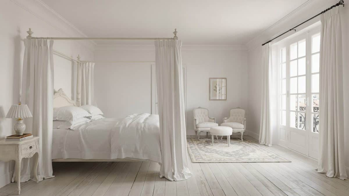 All white bedroom with slim four poster bed and painted white plank floor