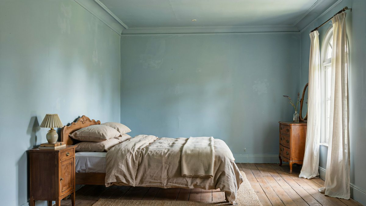 Soft blue bedroom with carved wood headboard and antique chest of drawers