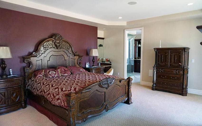 Bedroom with burgundy wall behind bed with ornate decorative details and griege wall paint