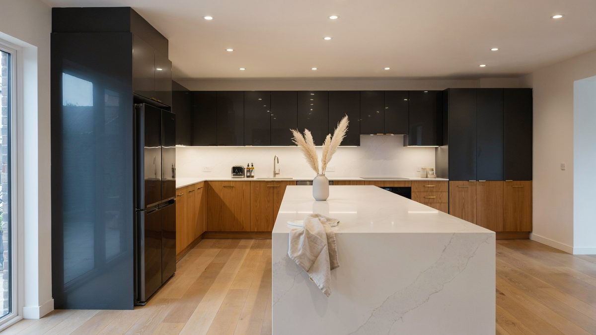 Black gloss wall units above light oak base cabinets with a white waterfall island