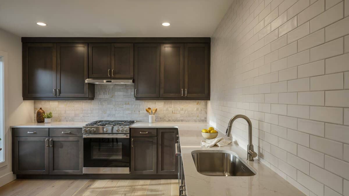 Dark stained cabinets meet a light stone tile backsplash and white subway side wall