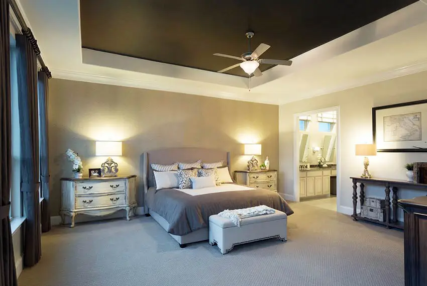 Bedroom with tan color walls, French style side tables and ceiling fan