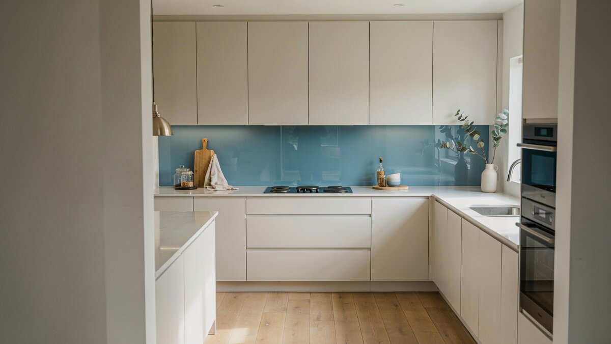 Seamless blue glass panel spans flat front cabinets in a bright modern kitchen