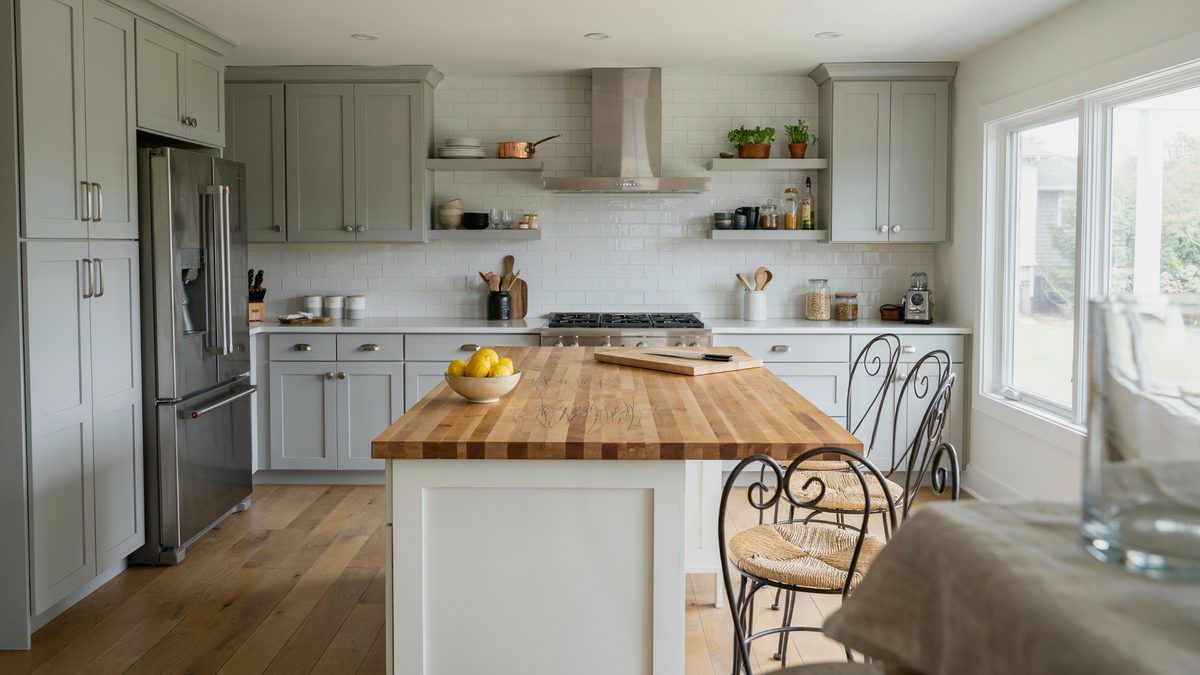 Soft gray perimeter cabinets around a white island topped in maple butcher block