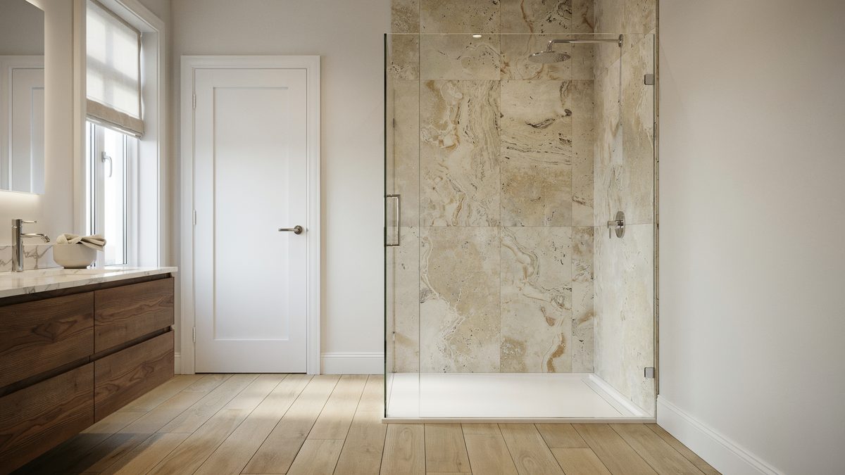 Frameless glass shower panel with veined travertine wall beside a wood vanity