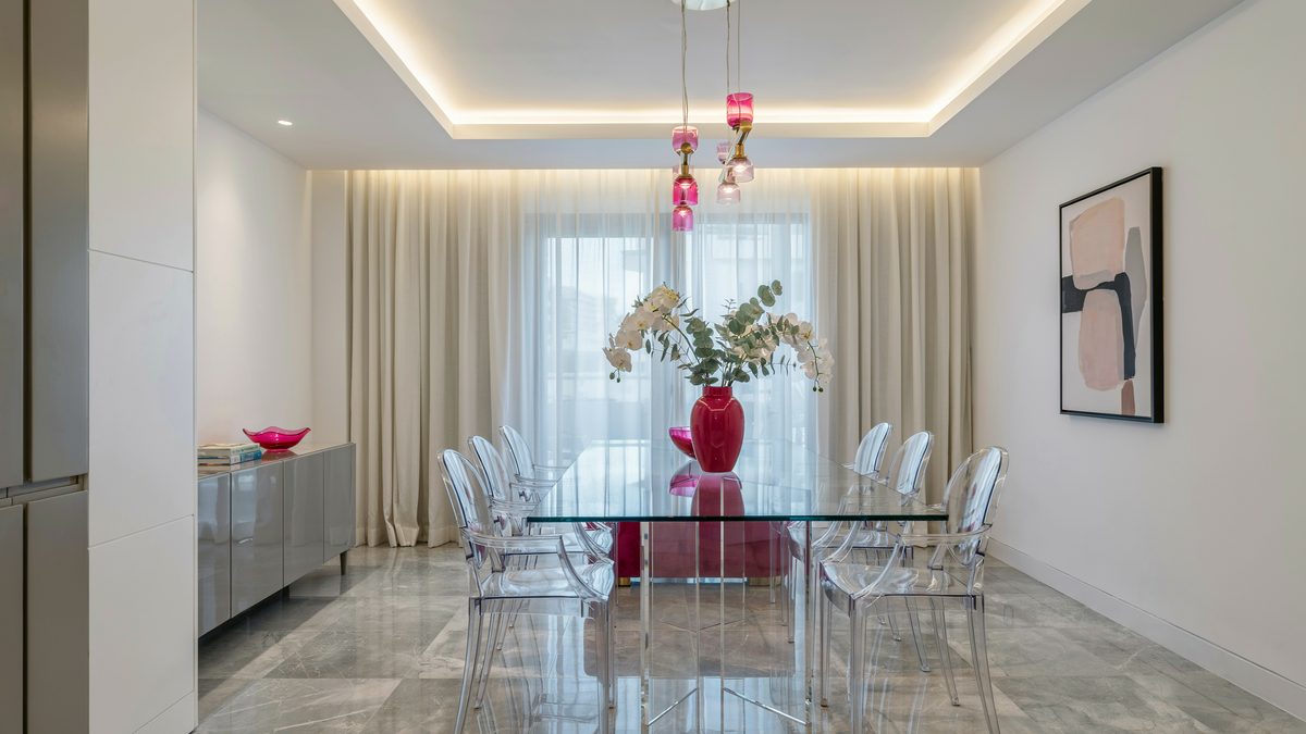 Clear acrylic chairs at a glass table under a glowing tray ceiling