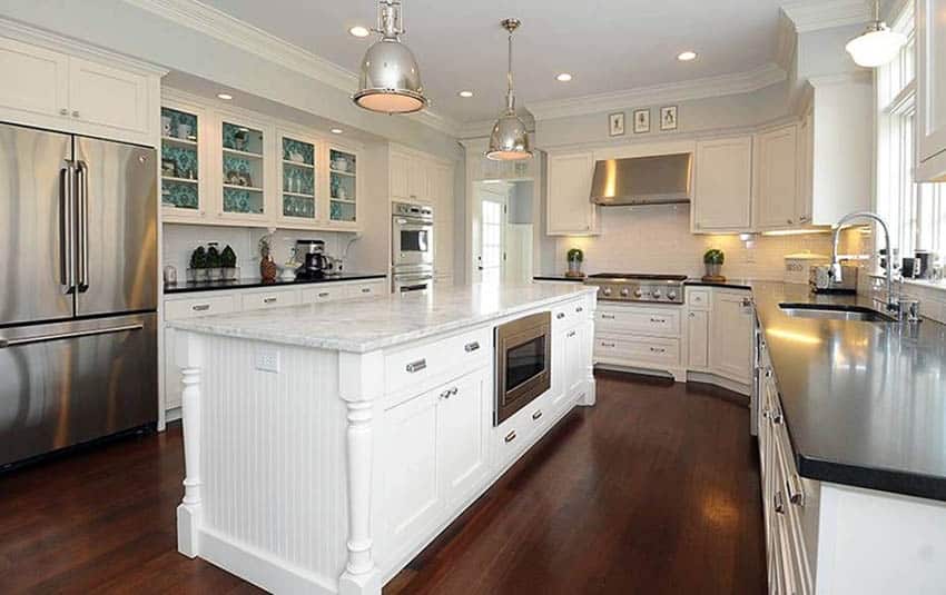 Kitchen with engineered wood floors, white cabinets, subway tile and marble counters