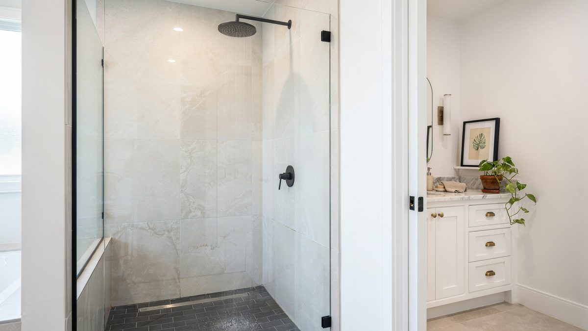 Narrow white travertine shower with black fixtures and dark subway floor tile