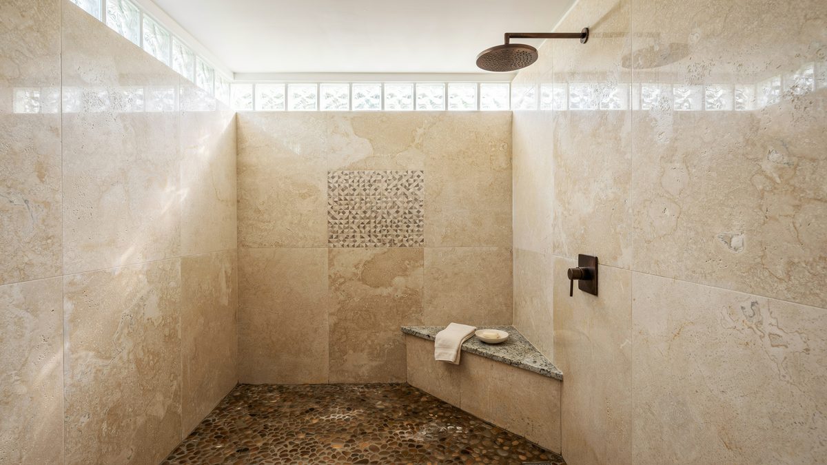 Glass block clerestory above a travertine shower with speckled stone bench