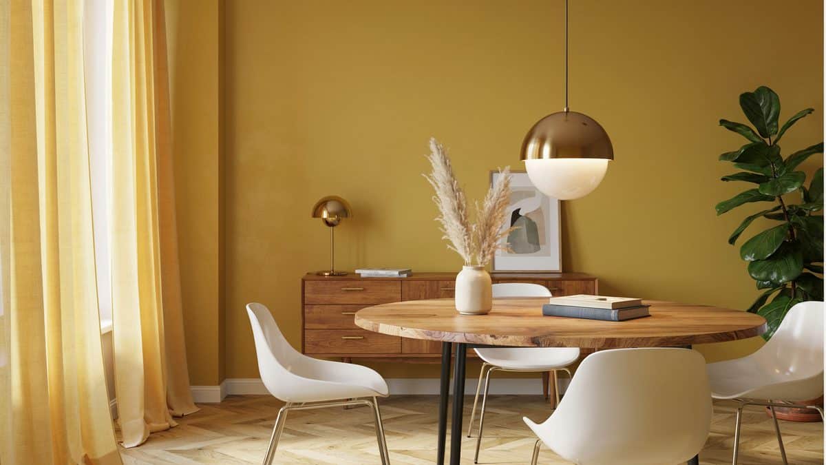 Round wood table and white chairs against a mustard yellow accent wall