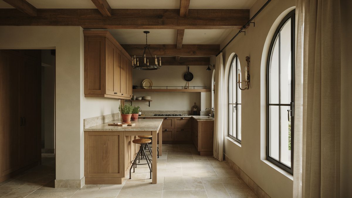 Iron chandeliers hang from a high beamed ceiling above beige granite counters
