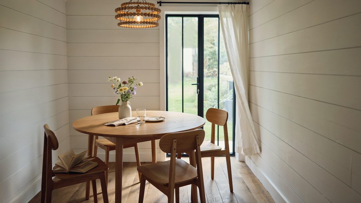 Round oak table beside a slim black metal door and beaded chandelier