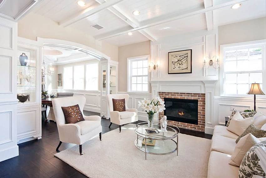 Traditional living room with hardwood flooring, wainscoting, tray ceiling and brick fireplace with white mantel