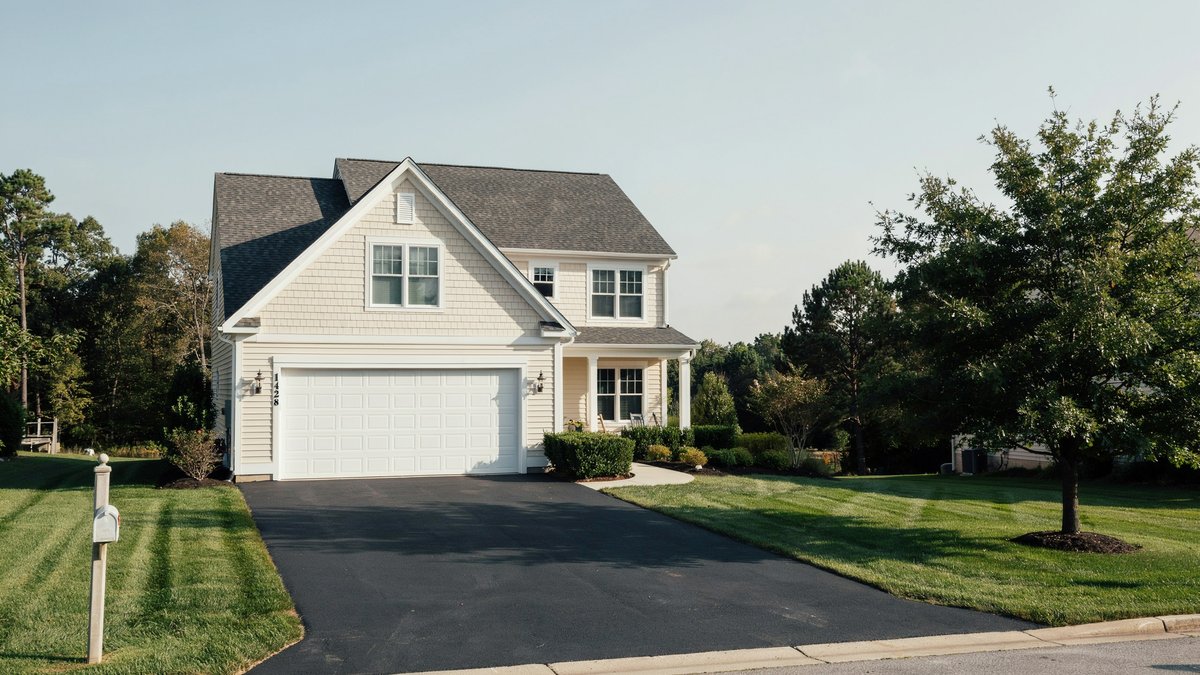 Black asphalt driveway curving to a white two story traditional home with attached garage