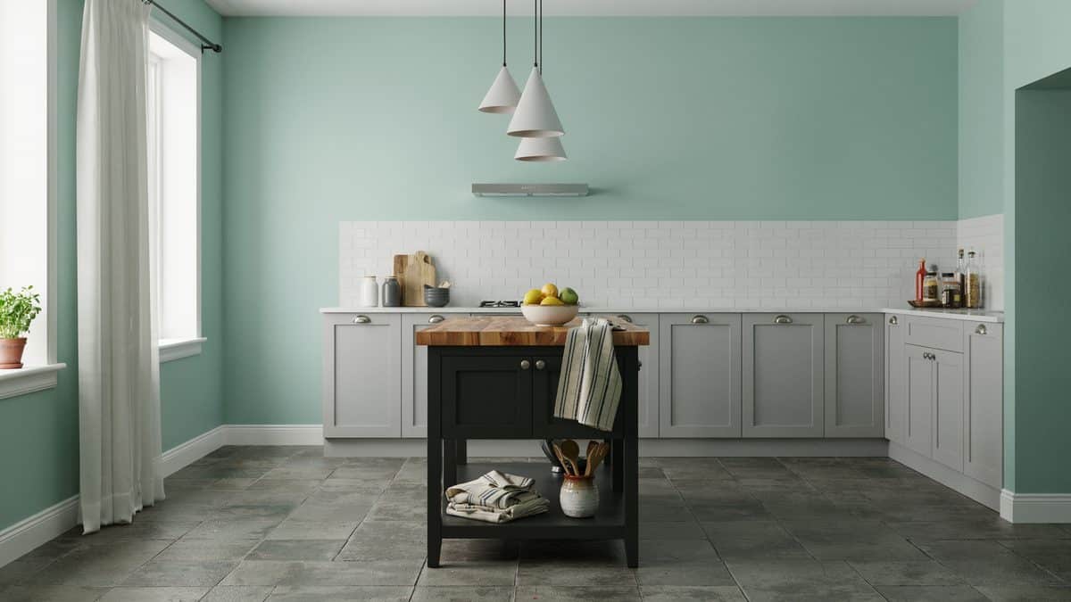Small black portable island with wood top against soft mint green kitchen walls