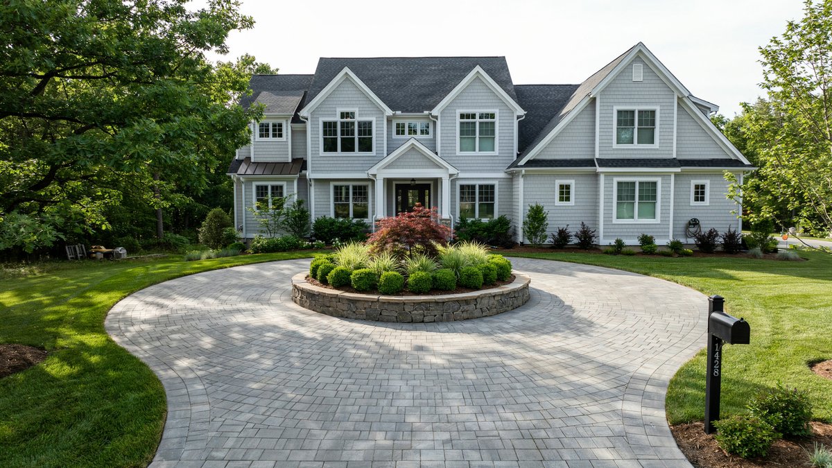 Gray paver circular driveway looping a raised planter island at a shingle style home