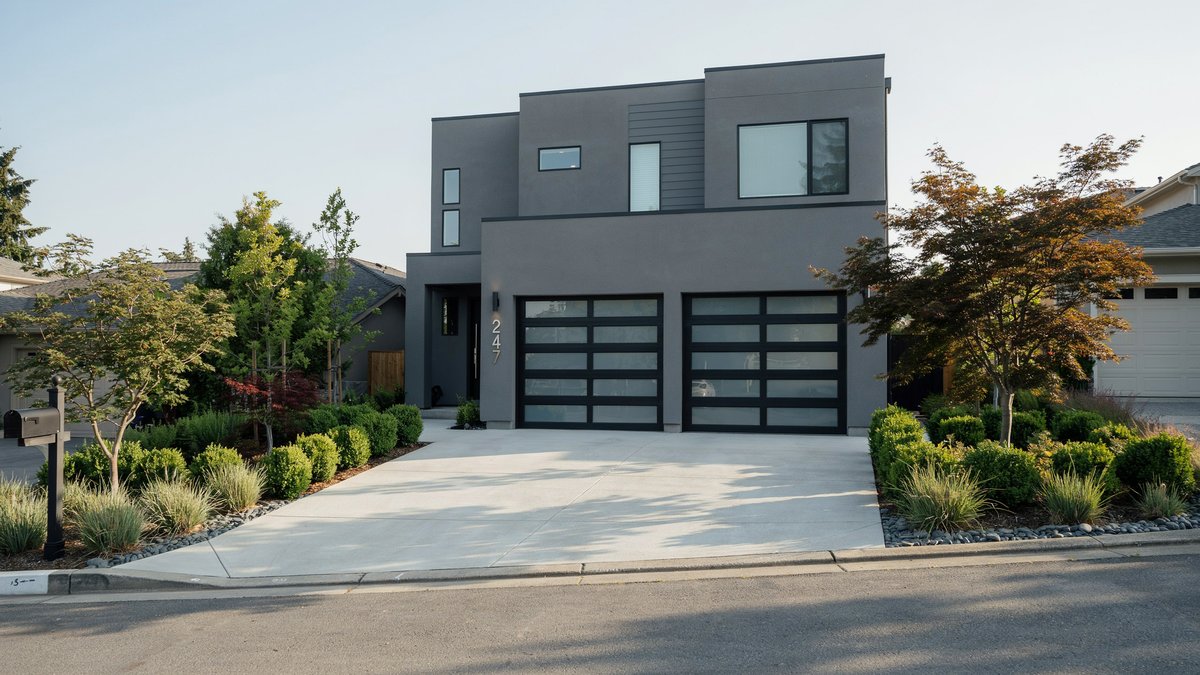 Wide poured concrete driveway leading to a dark gray modern house with glass garage doors