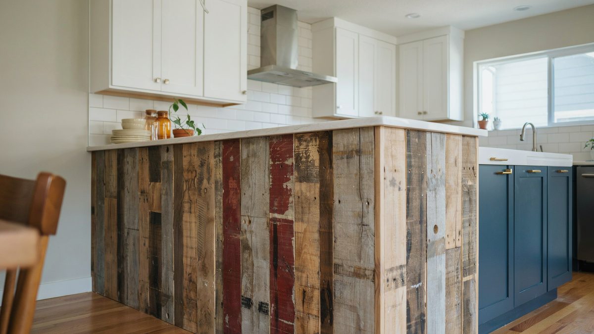 Multi colored salvaged plank peninsula joining navy blue base cabinets and farmhouse sink