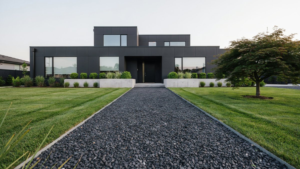 Dark crushed basalt gravel cutting through a manicured lawn at a black modern house