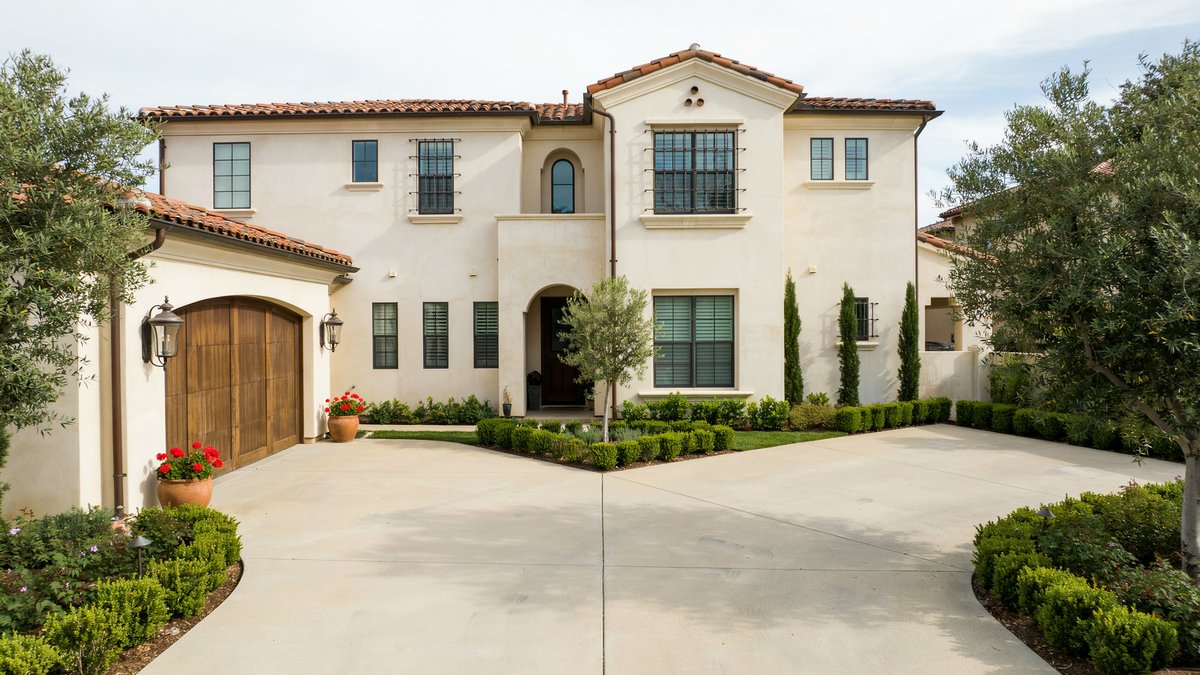 Broad concrete driveway splitting toward the arched garage of a Tuscan style stucco estate