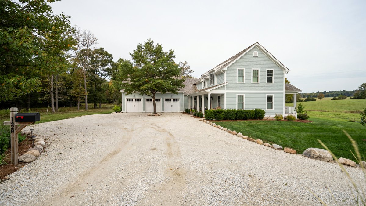 Gravel drive with stone edging leading to a green three car country home