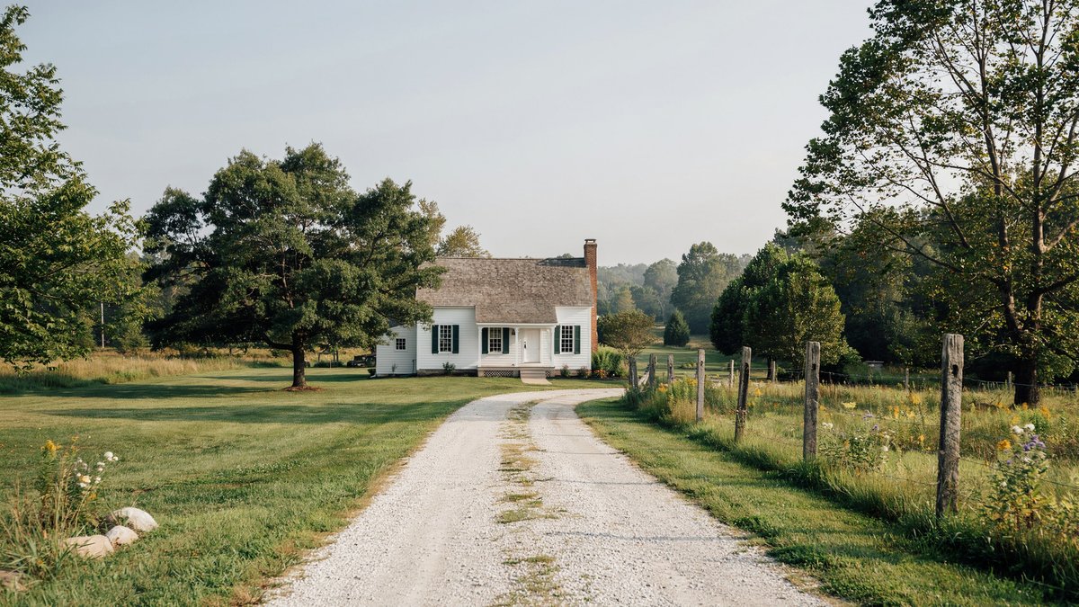 Pale gravel driveway lined with wooden fence posts leading to a white country house