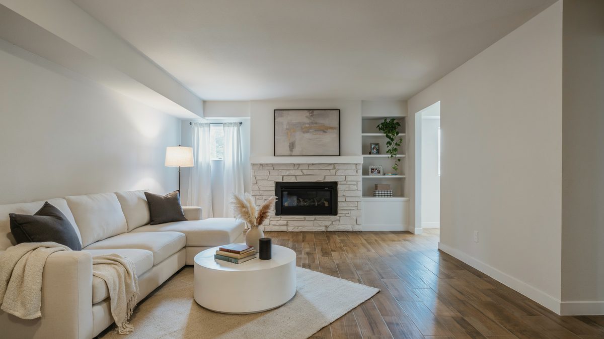 Wood look porcelain planks leading through a white basement lounge toward a stone fireplace