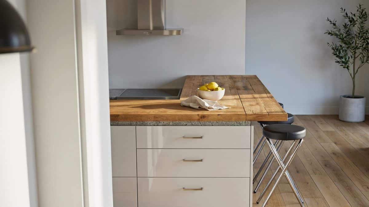 Wood plank counter overhang above glossy white drawers with backless chrome stools