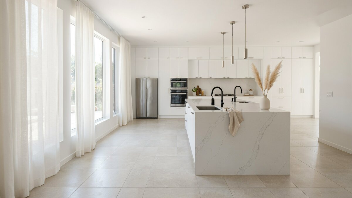 Open all white kitchen with a marble island, tile floors and a stainless refrigerator