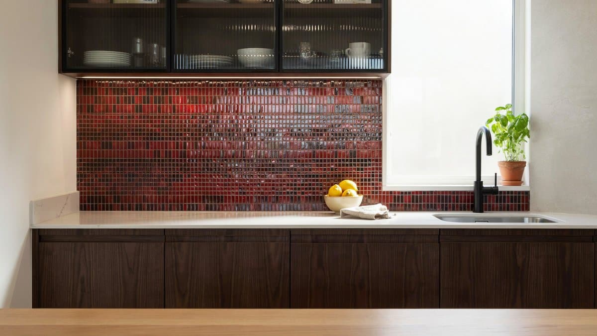 Dark wenge cabinets under a red and black mosaic tile backsplash