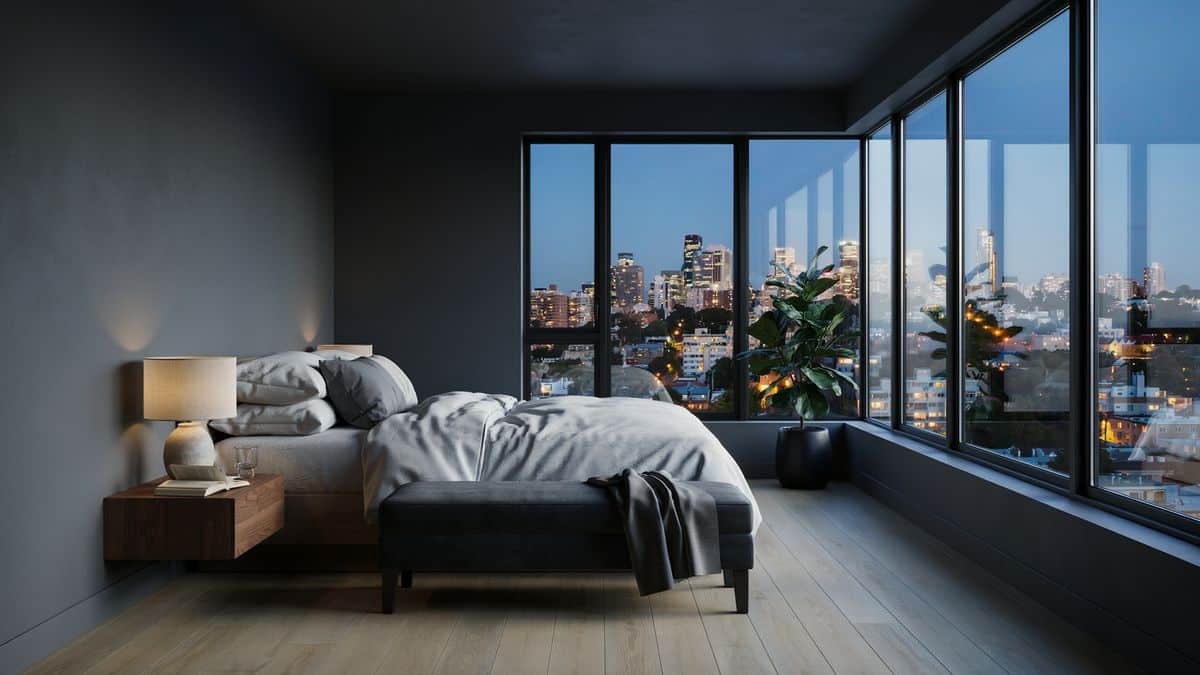 Dark gray bedroom with wrap around corner windows and evening city view