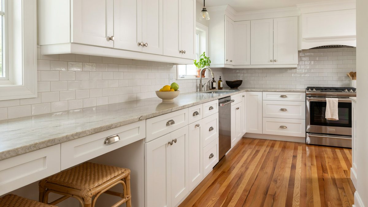 Subway tile backsplash runs behind pale granite counters and oak flooring