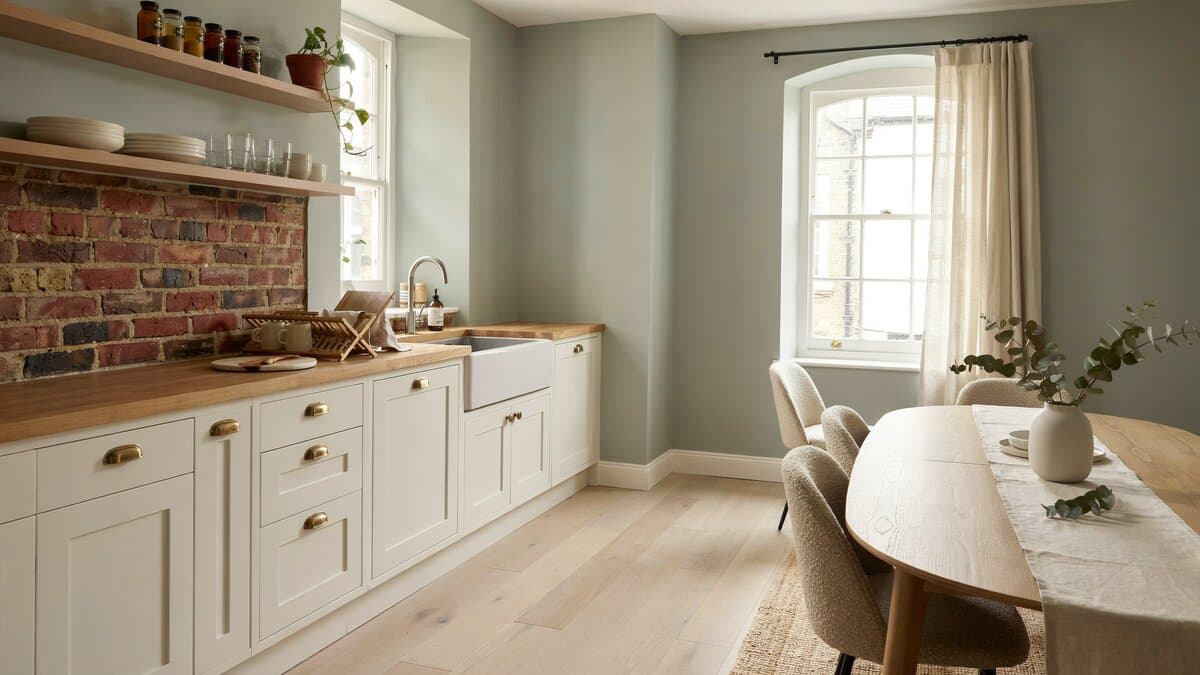 Muted sage walls and brick backsplash beside an open dining area with upholstered chairs