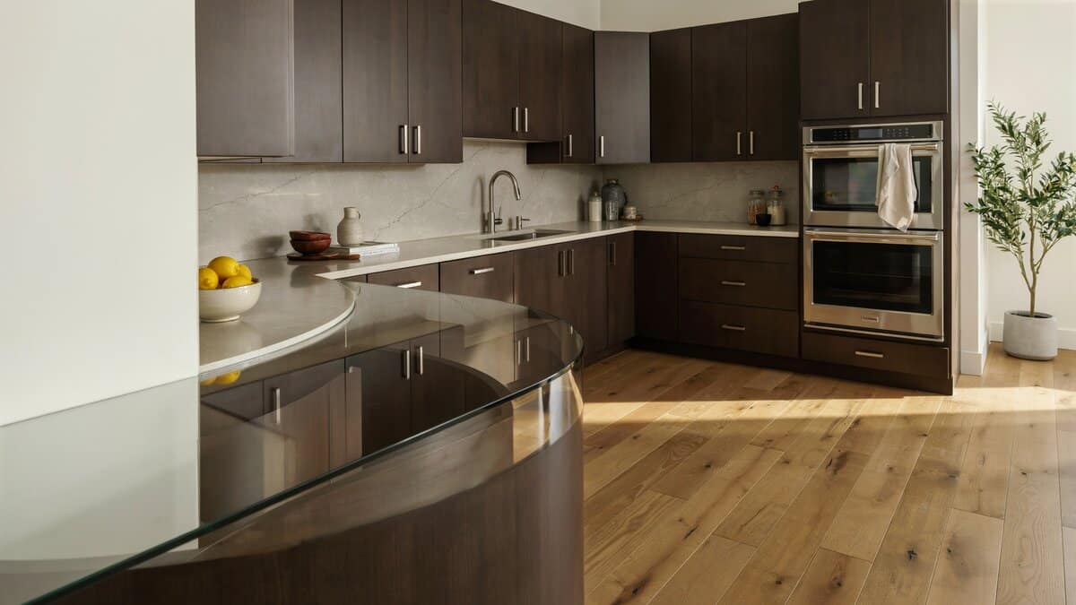 Curved glass topped peninsula joining dark brown cabinets above pine wood floors