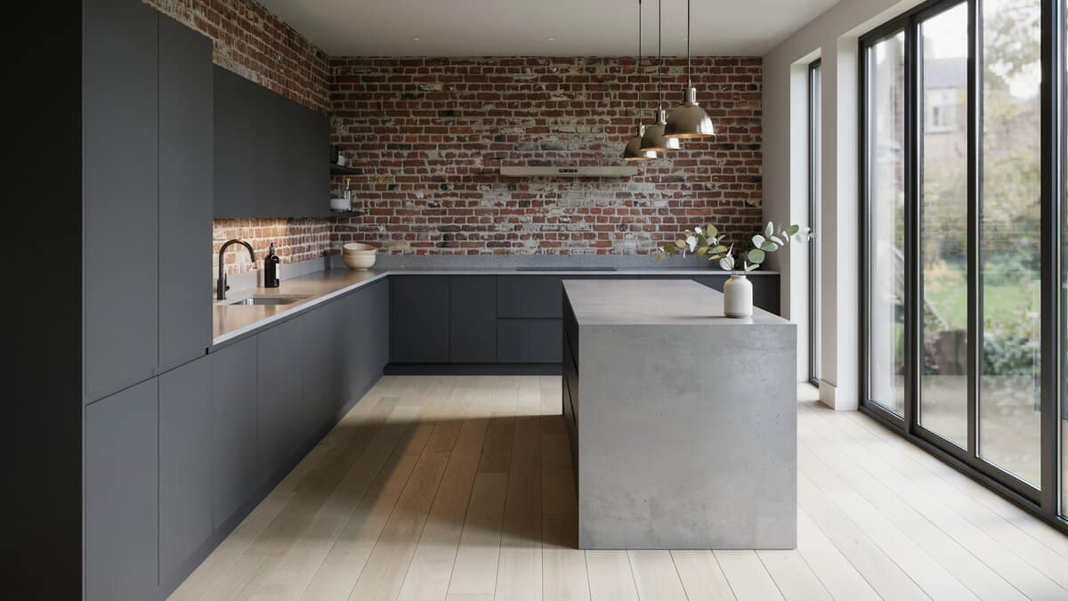 Exposed red brick wall behind charcoal cabinets with a polished concrete island beside glass doors