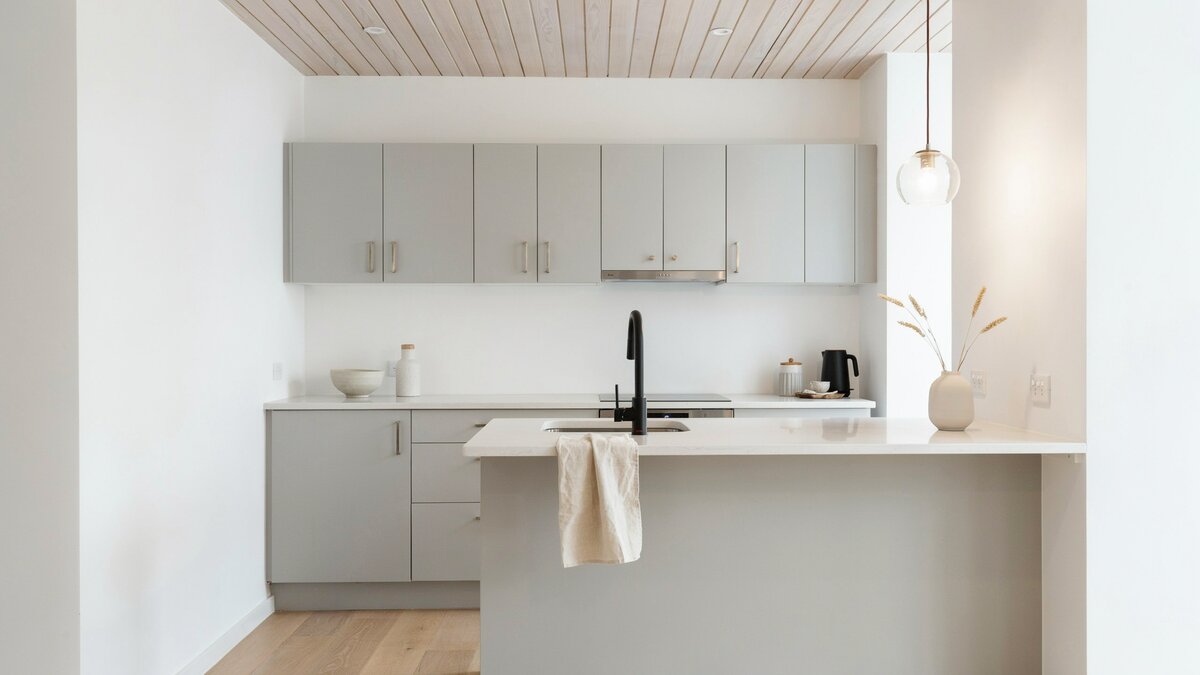 Bleached wood slat ceiling above gray flat panel cabinets in a compact white kitchen