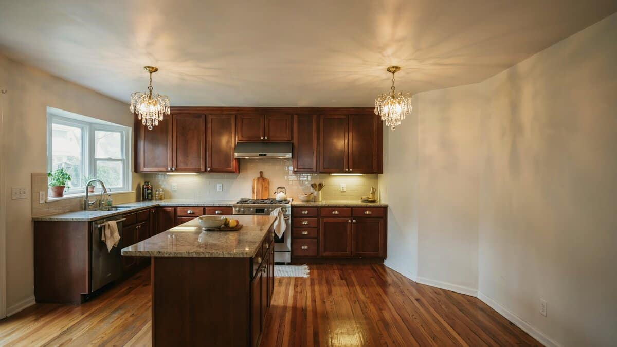 Ornate chandeliers above dark stained cabinets, off white walls and beige tile backsplash