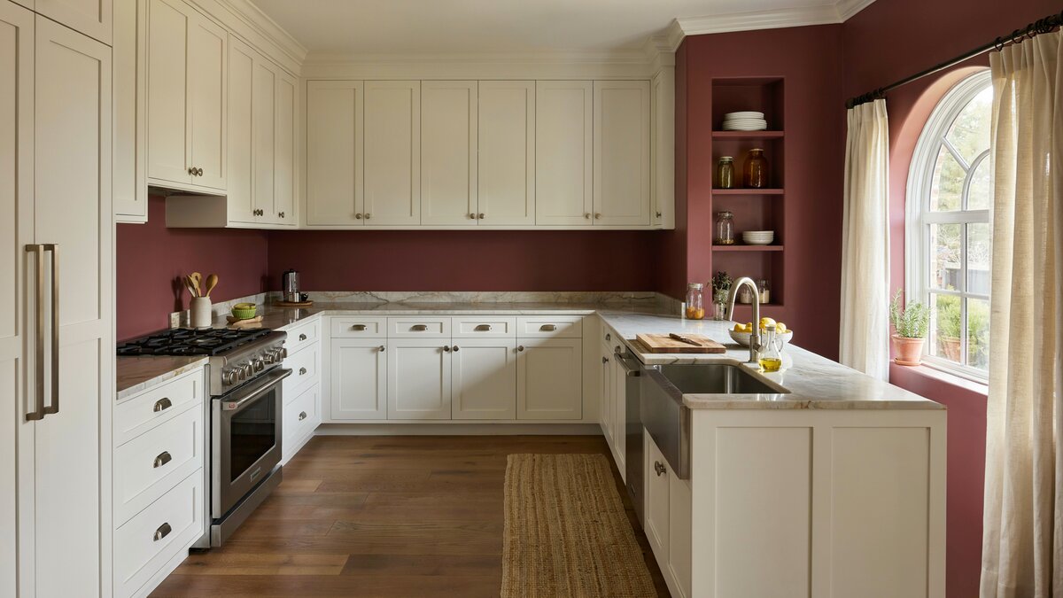 Deep burgundy walls surrounding white raised panel cabinets in a traditional layout